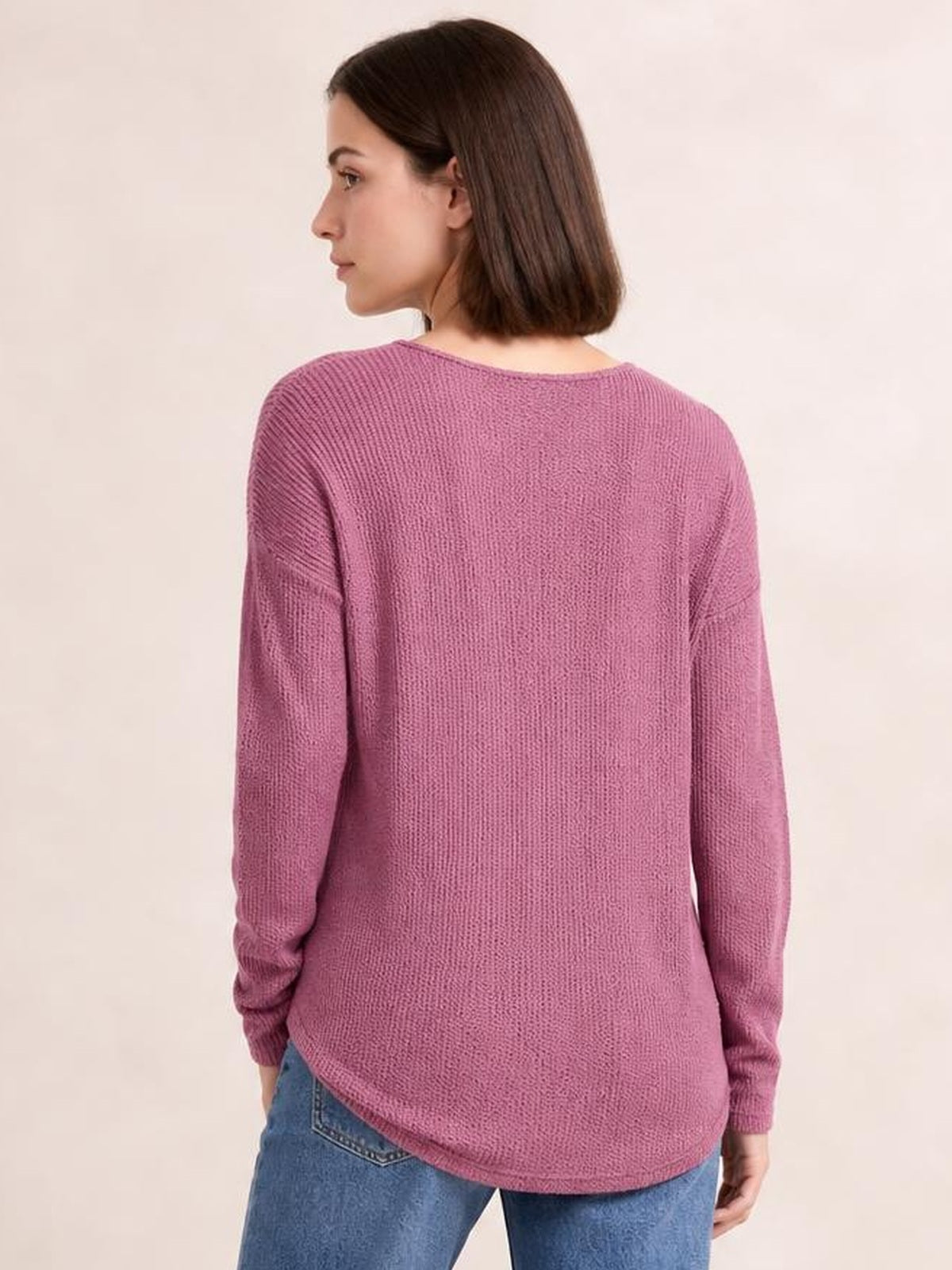 A model wears a mauve pink long sleeve T-shirt with a textured knit finish, relaxed loose silhouette, rounded hem, and ribbed cuffs in a back three-quarter pose.