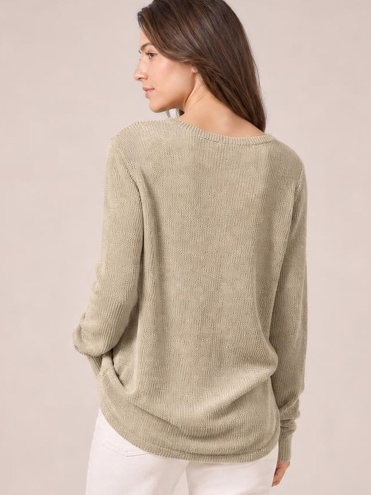 A model wears a beige long sleeve T-shirt with a relaxed, softly draped silhouette, rounded neckline, and textured knit construction in a turned-back pose.