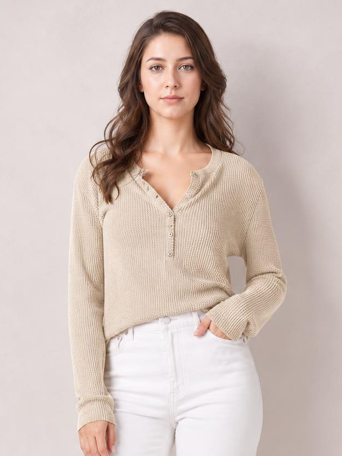 A model wears a beige long-sleeve T-shirt with a notched neckline, button placket, textured knit construction, and a relaxed silhouette, posing with one hand in her pocket.