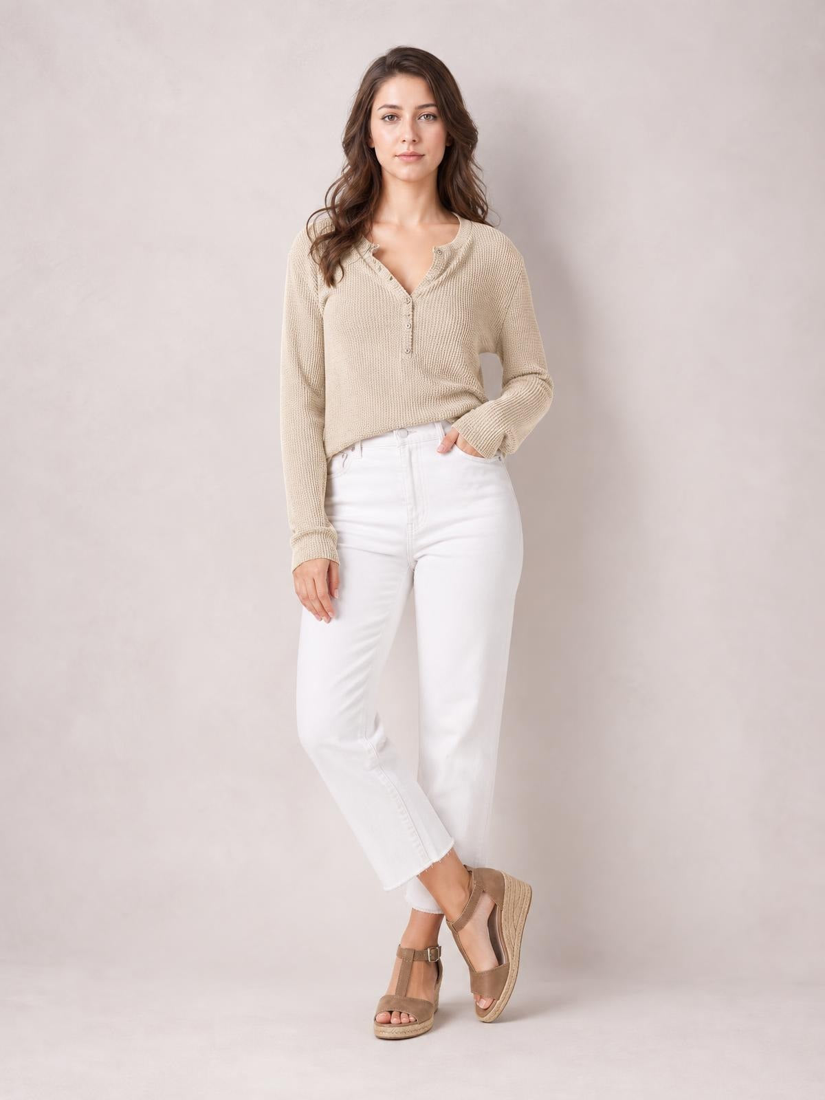 Model wears a beige notched long-sleeve T-shirt with a buttoned V-neck placket, textured knit construction, relaxed silhouette, and one hand in her pocket.