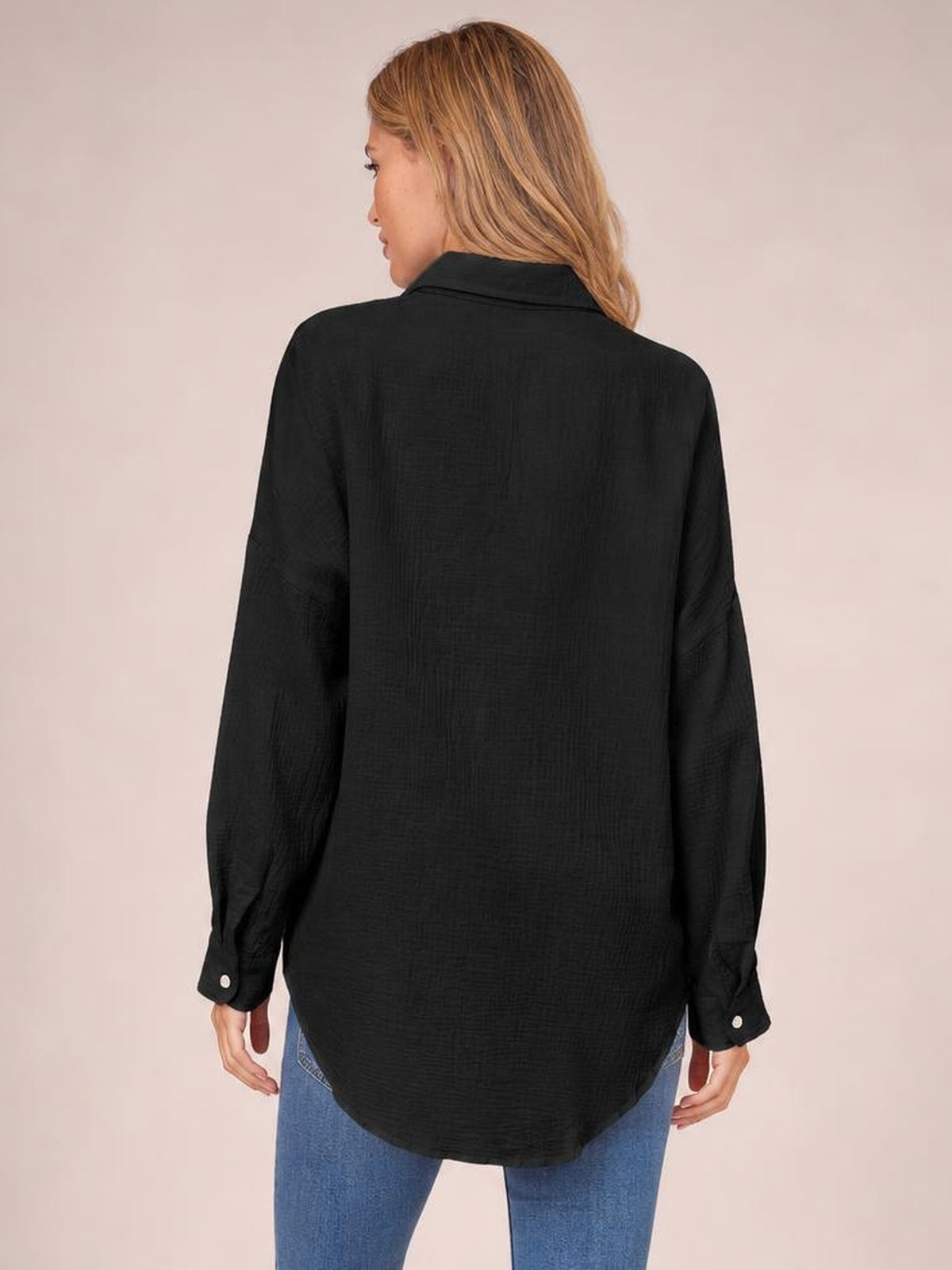Model shown from the back wearing a black textured button-up shirt with a relaxed silhouette, long sleeves, curved hem, and buttoned cuffs.