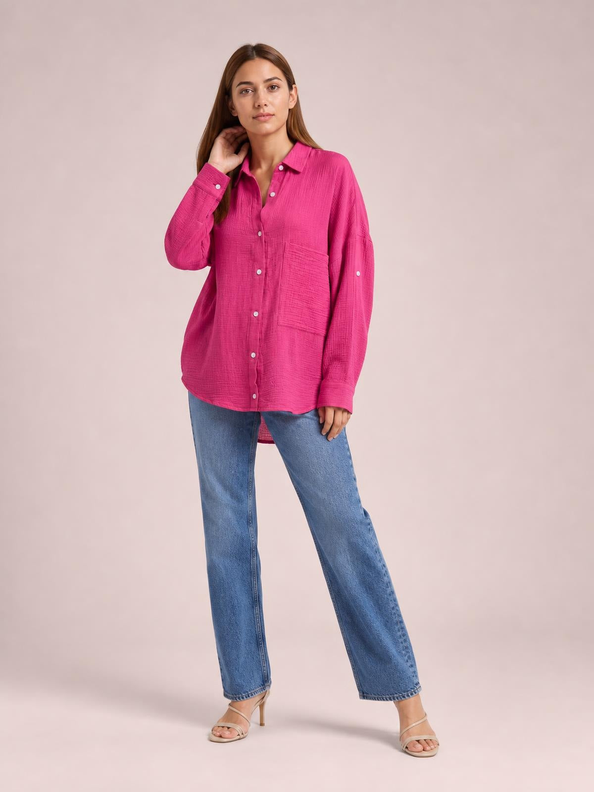 A model poses in a bright pink textured button-up shirt with a collar, long sleeves, front patch pockets, and a relaxed tunic-length silhouette.