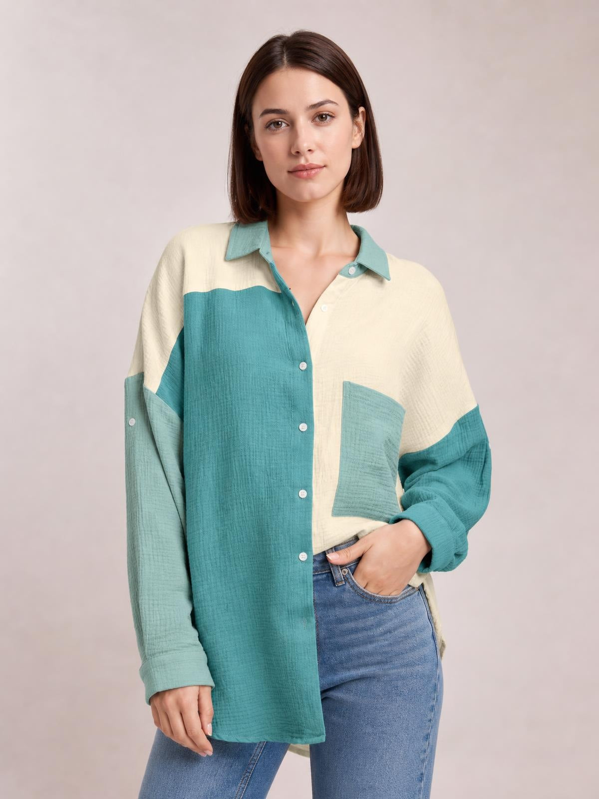 A model wears a relaxed, longline textured button-up shirt in cream and teal with a pointed collar, button front, long sleeves, and a patch pocket, posing with one hand in her jeans pocket.