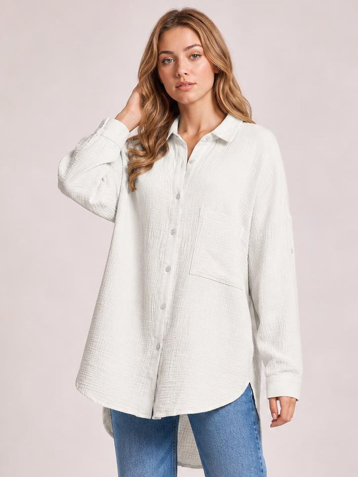 A model poses in a white textured button-up shirt with long sleeves, a relaxed oversized silhouette, front buttons, and a visible chest pocket.
