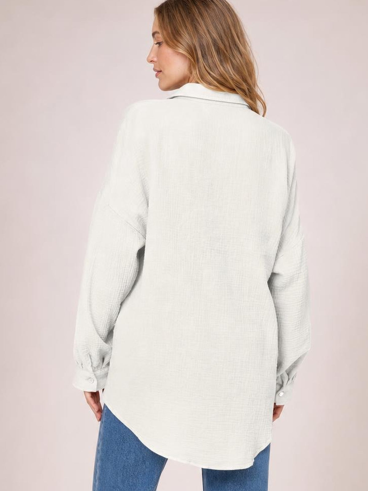 A model looks over her shoulder wearing a white textured button-up shirt with a relaxed silhouette, long sleeves, button cuffs, and a curved hem.