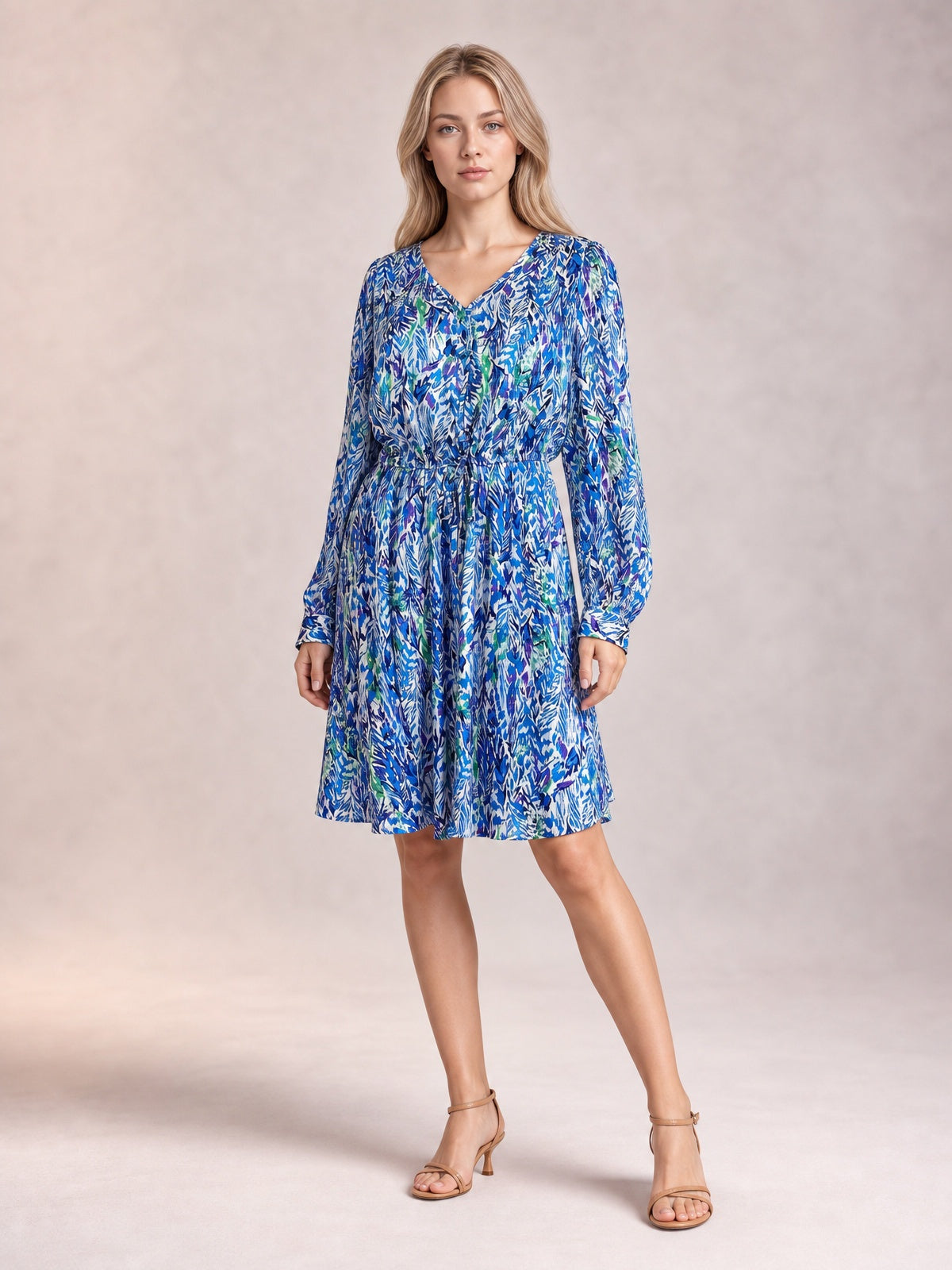 A model poses in a blue, green, and white printed long-sleeve dress with a V-neck, ruched drawstring waist, button front, and gently flared knee-length skirt.