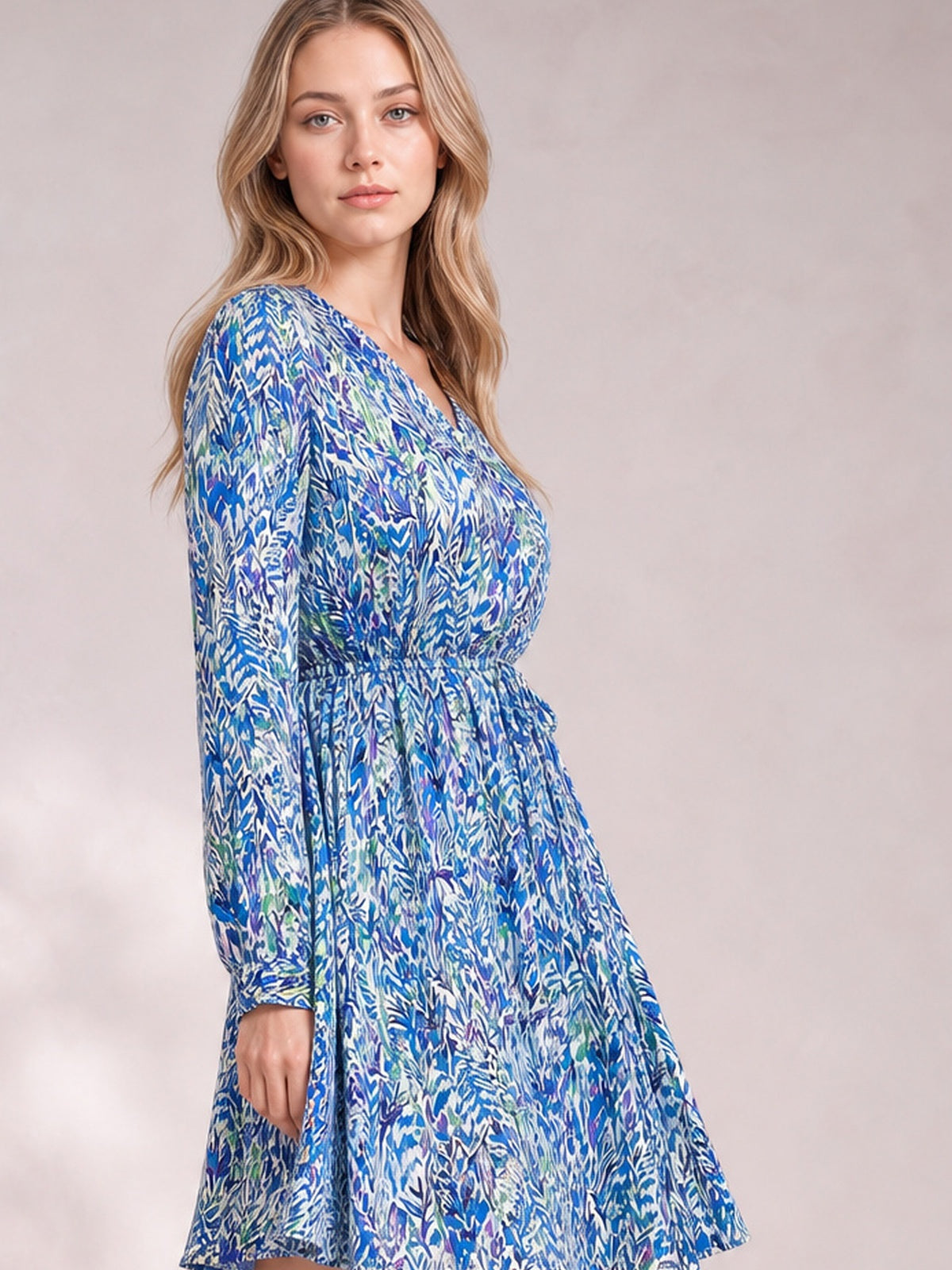 A model poses in a blue and white printed long-sleeve dress with a V-neck, ruched drawstring waist, and fluid gently flared skirt.