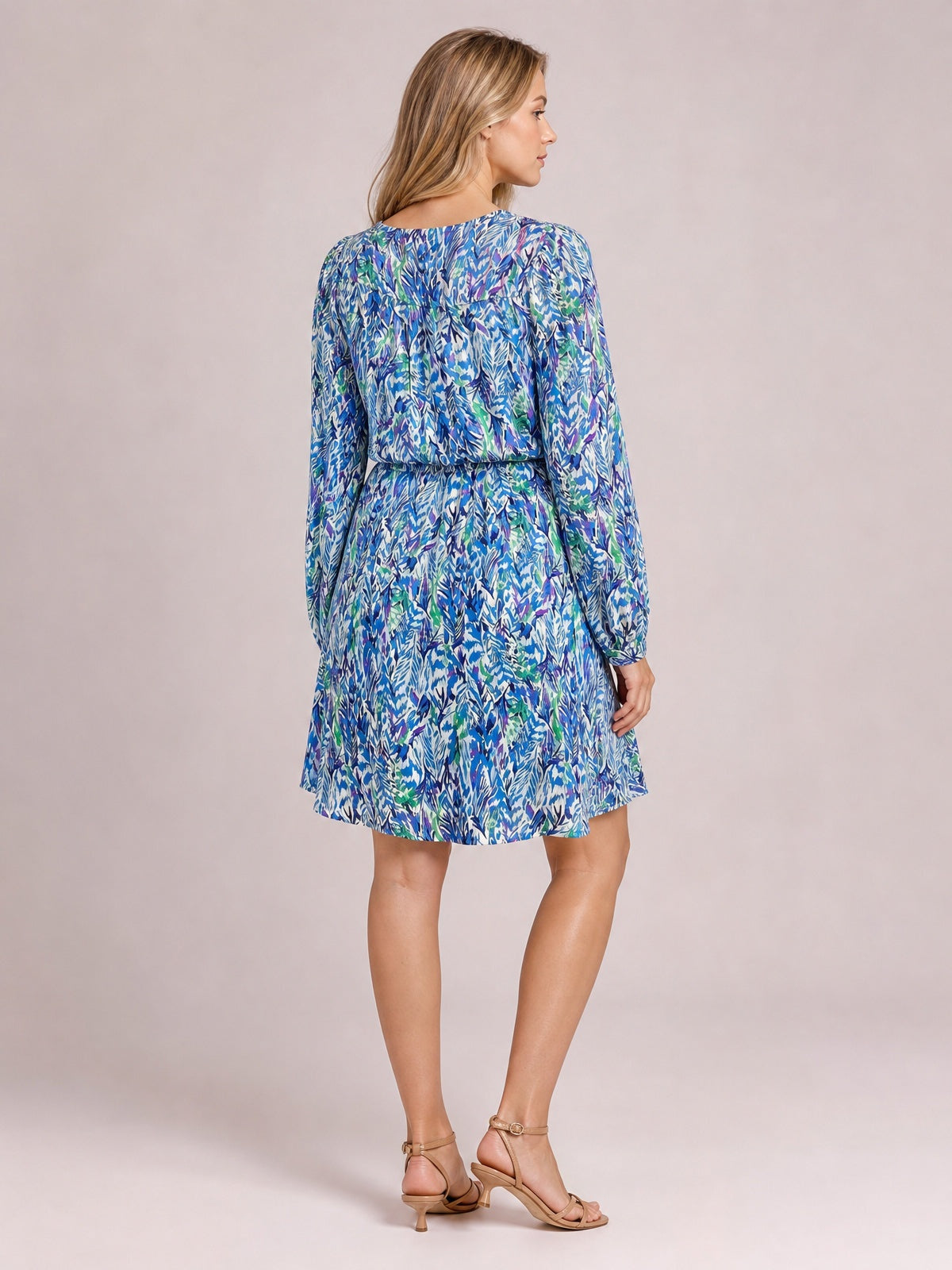 A model poses in a blue, green, and white printed long-sleeve dress with a drawstring waist, gathered bodice, and gently flared skirt.