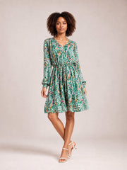 Model poses in a green botanical-print long-sleeve dress with a V-neck, ruched drawstring waist, buttoned front, and gently flared skirt.