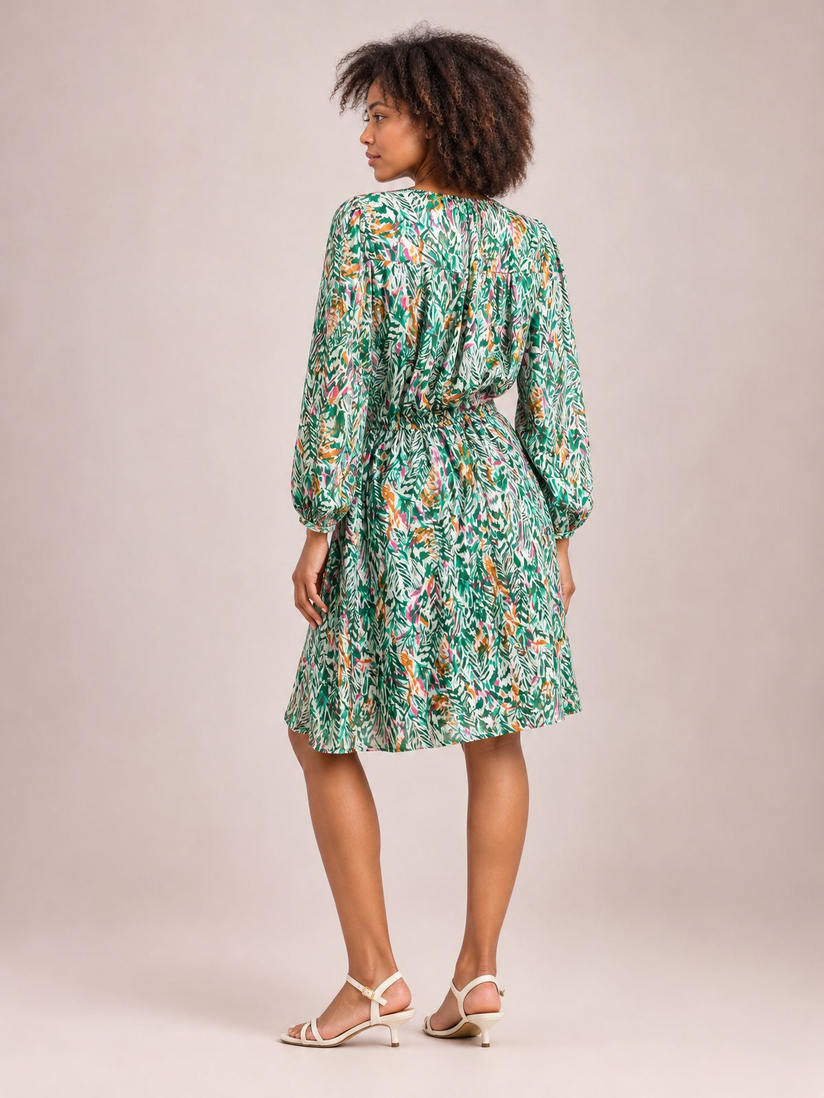 Model poses in a green, orange, and white printed long-sleeve dress with ruched drawstring waist, buttoned detailing, and a gently flared knee-length skirt.