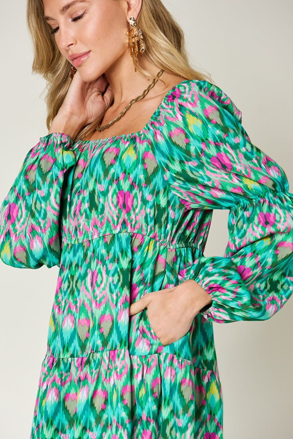 A model poses in a vibrant green and pink printed long sleeve dress with gathered neckline, voluminous sleeves, ruched waist, and an easy A-line silhouette.