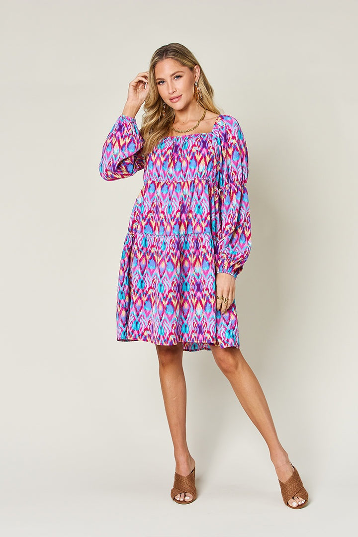 A model poses in a vibrant multicolor printed long sleeve dress with gathered waist detailing, voluminous sleeves, and a relaxed A-line silhouette.