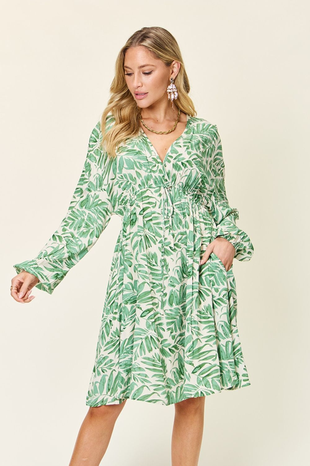 Model poses in a light green leafy-print dress with a V-neckline, ruched waist, voluminous balloon sleeves, and a relaxed above-knee silhouette.