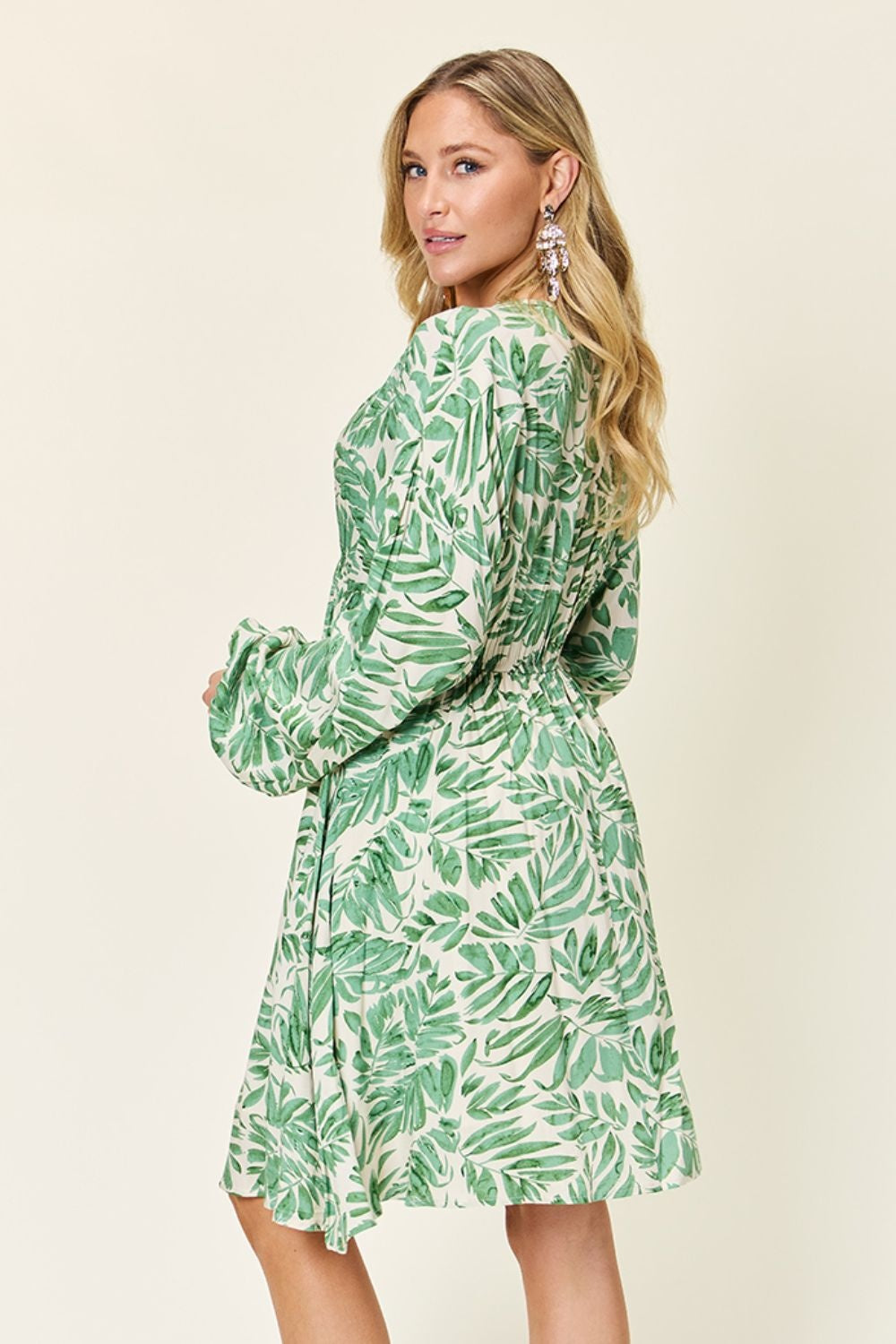 Model poses in a leafy light green printed dress with ruched waist, voluminous balloon sleeves, and a softly flared silhouette.
