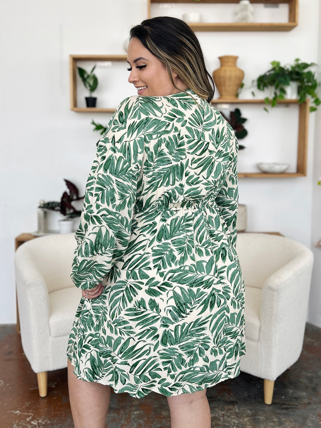 Model looks over her shoulder in a light green leafy-print dress with ruched waist, voluminous balloon sleeves, and a softly flared silhouette.