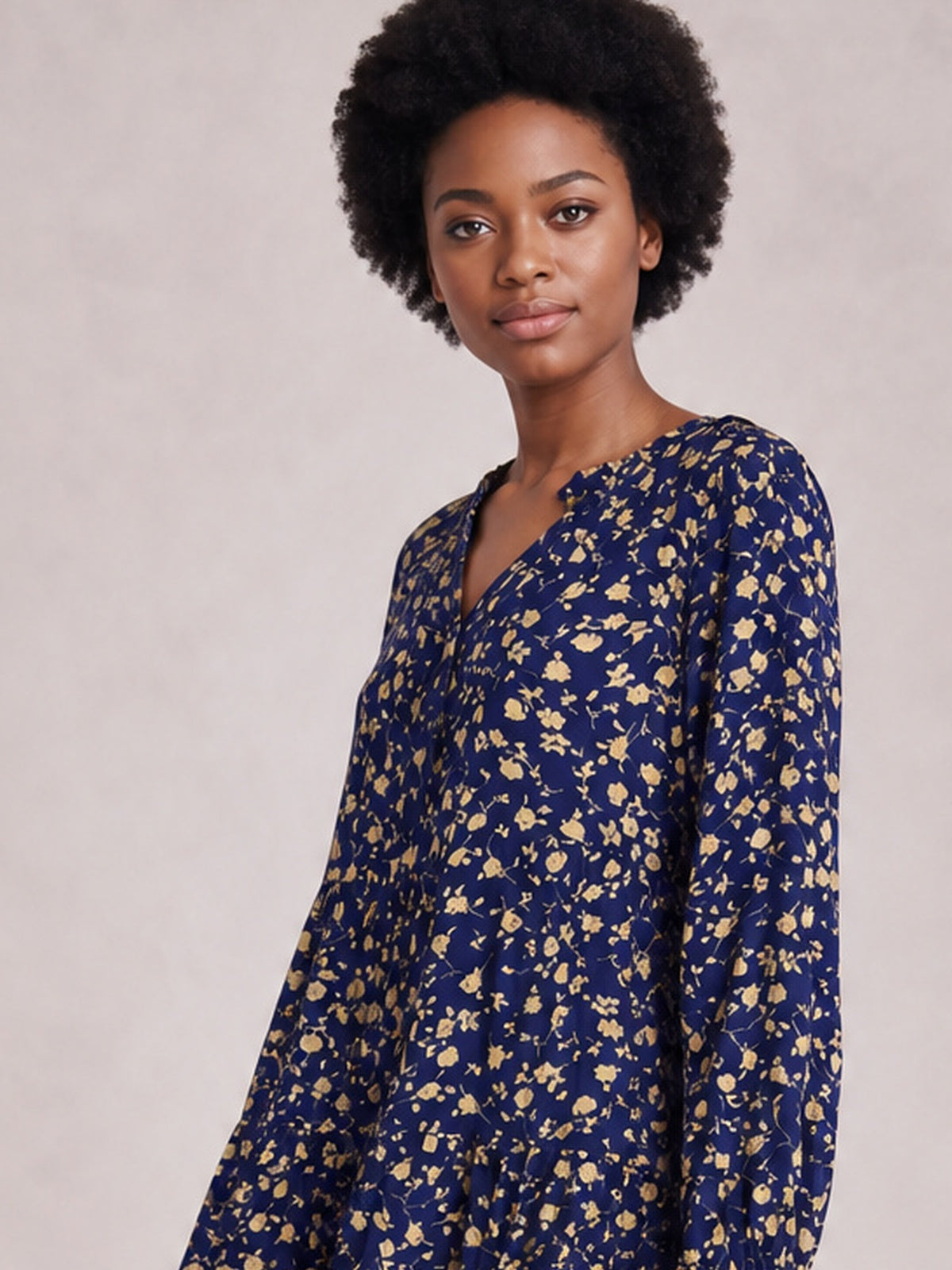 Model stands at an angle in a navy printed dress with scattered floral motifs, long sleeves, a tied V-neckline, and a softly flowing silhouette.