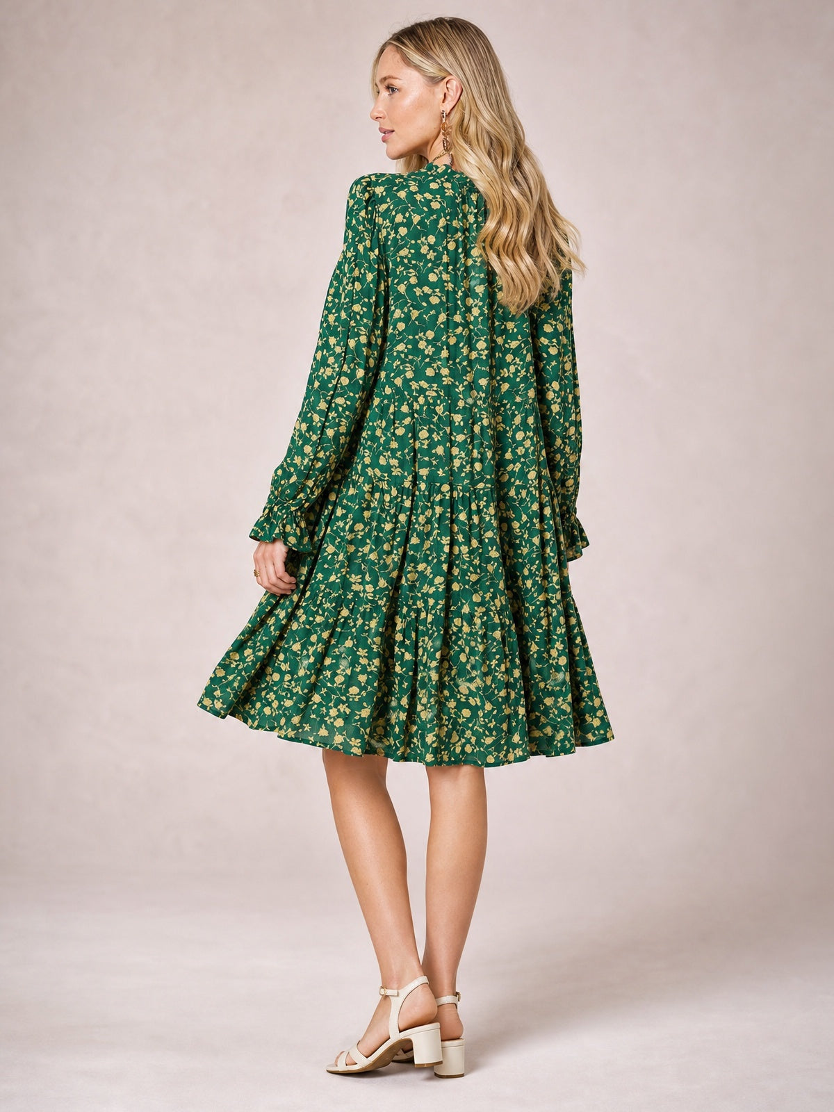 Model shown from behind in a green floral printed dress with long sleeves, a flowy tiered silhouette, gathered skirt, and ruffled hem.