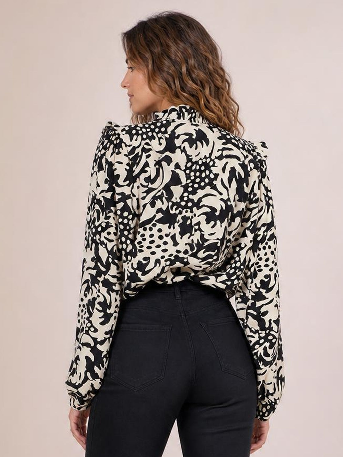 Model shown from the back wearing a black-and-cream printed shirt with ruffle-trimmed collar and voluminous balloon sleeves, tucked into dark high-waisted jeans.
