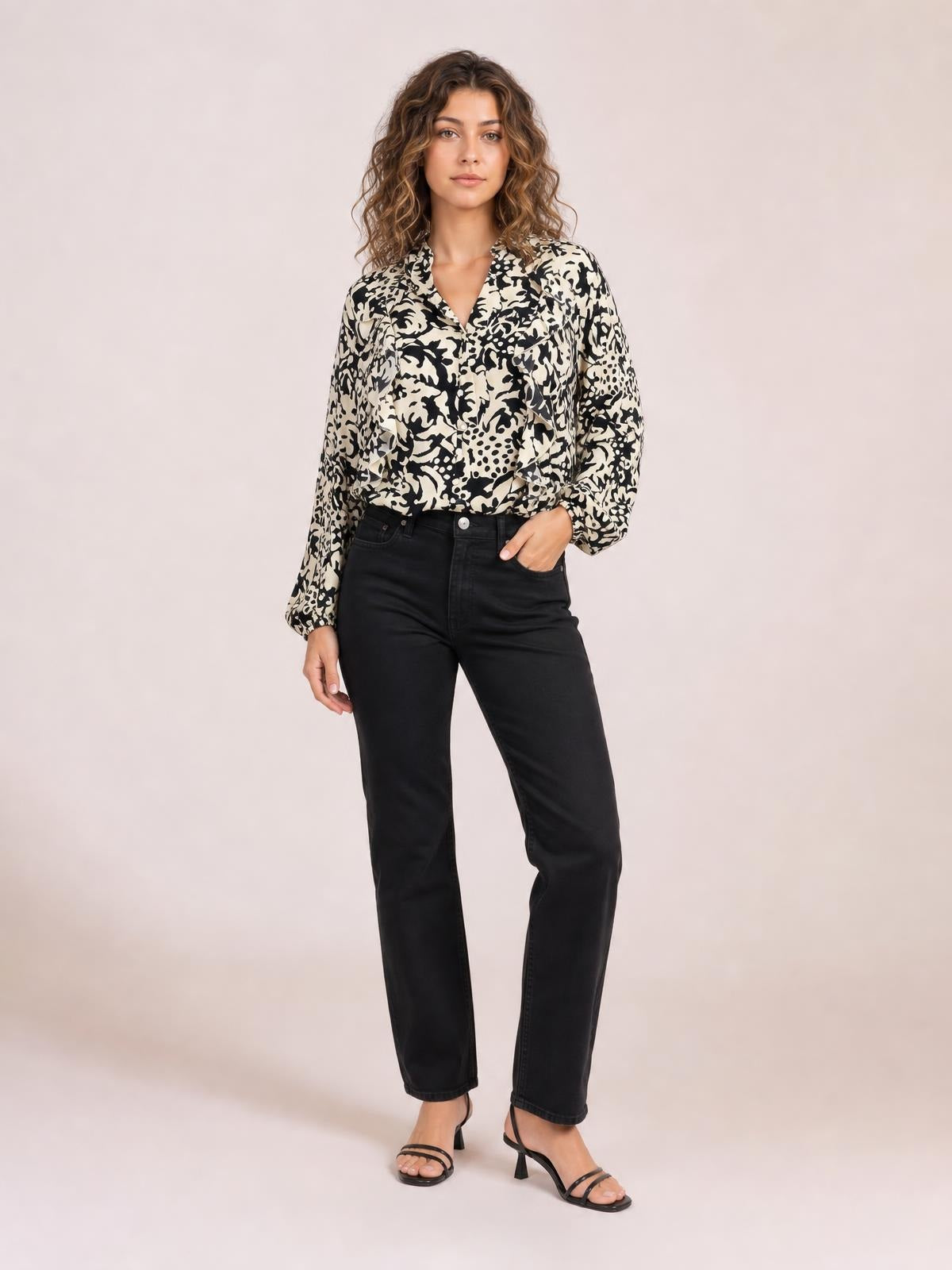 Model stands with one hand in her pocket wearing a cream-and-black printed shirt with ruffle trim, button front, and voluminous balloon sleeves.