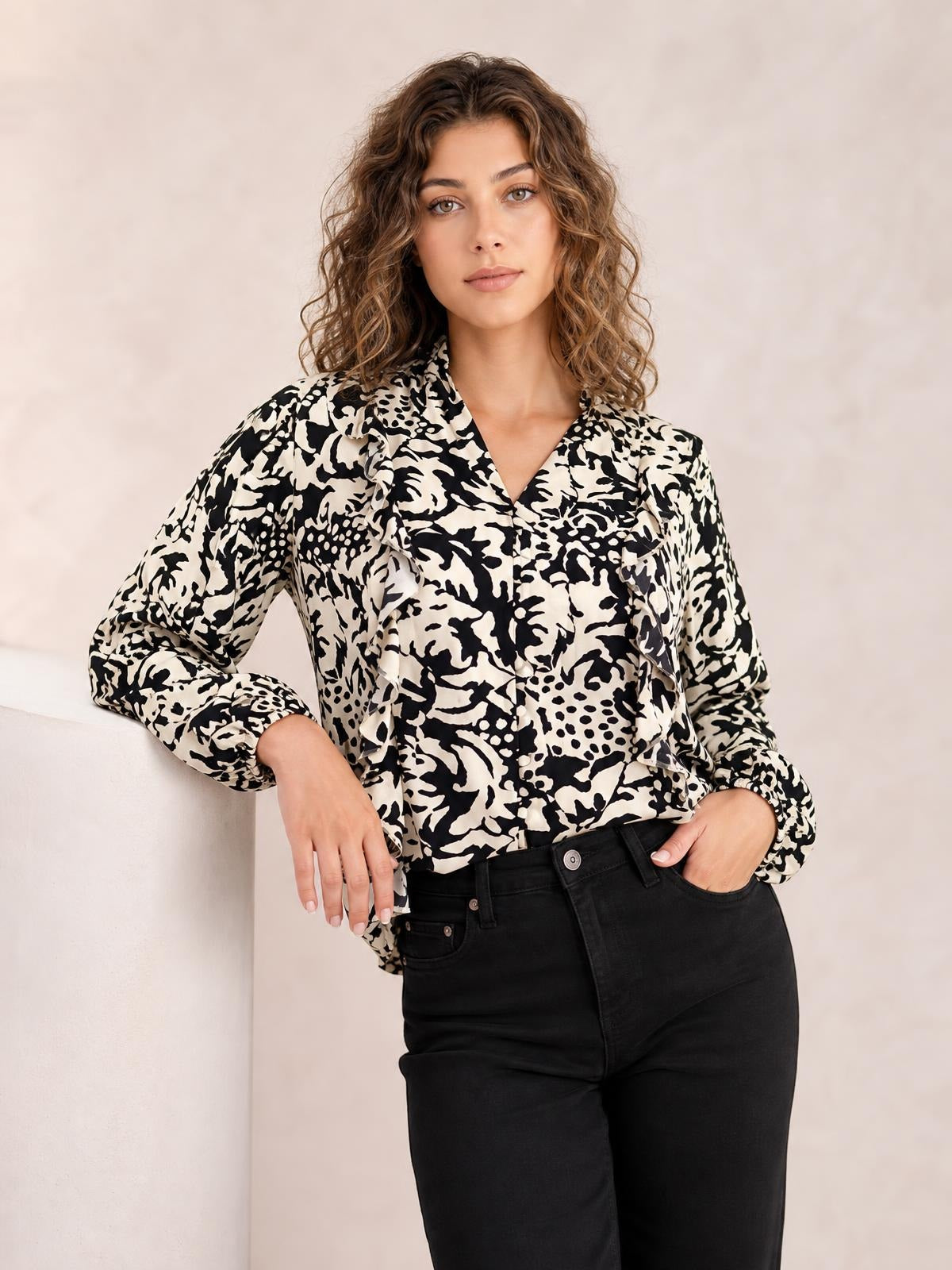 A model wears a black-and-cream printed shirt with ruffle trim, button front, and voluminous balloon sleeves, posing with one hand on her hip.