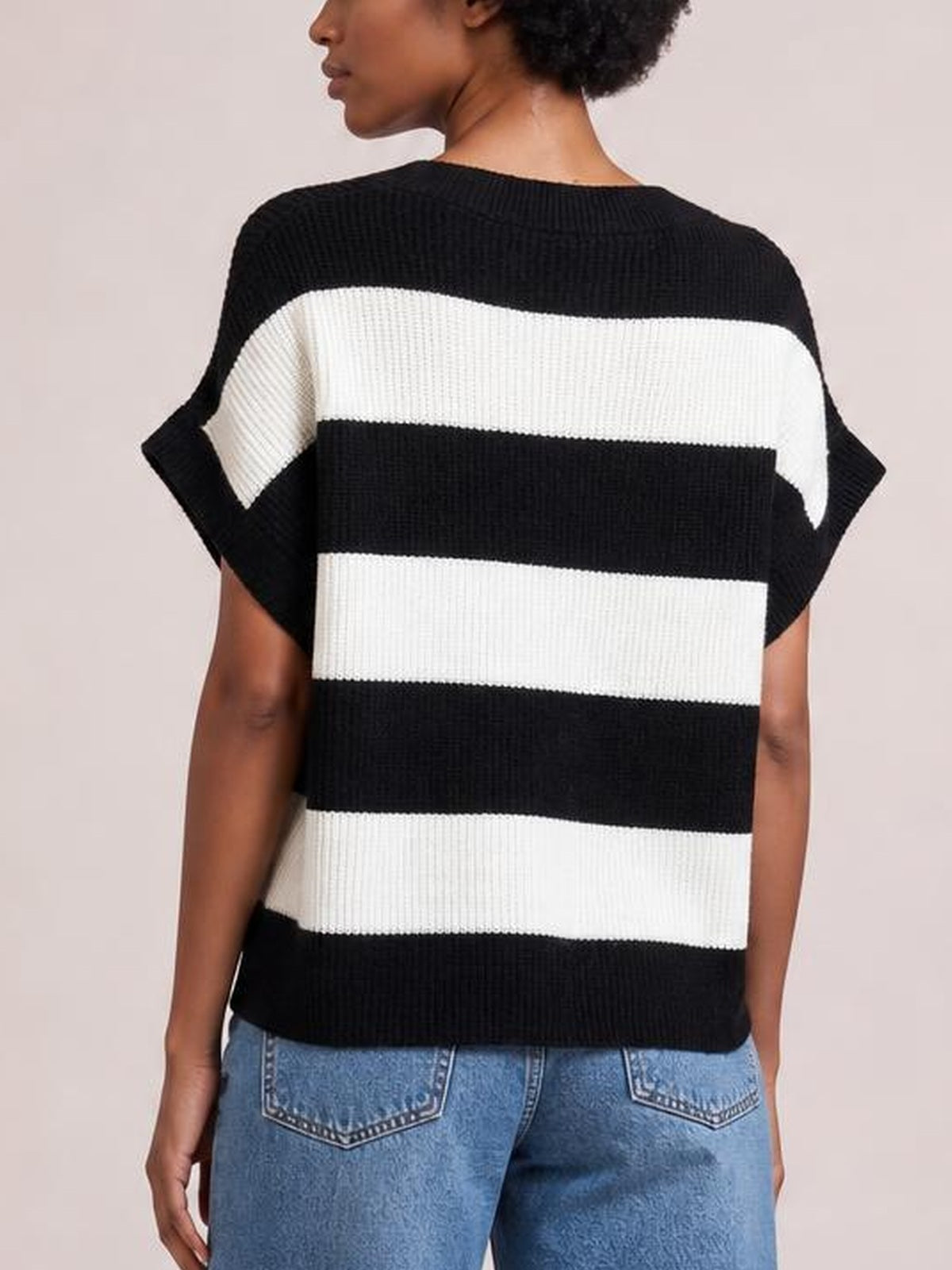 Back view of a model wearing a black-and-white striped short sleeve sweater with a relaxed silhouette, ribbed knit construction, and horizontal color-block bands.
