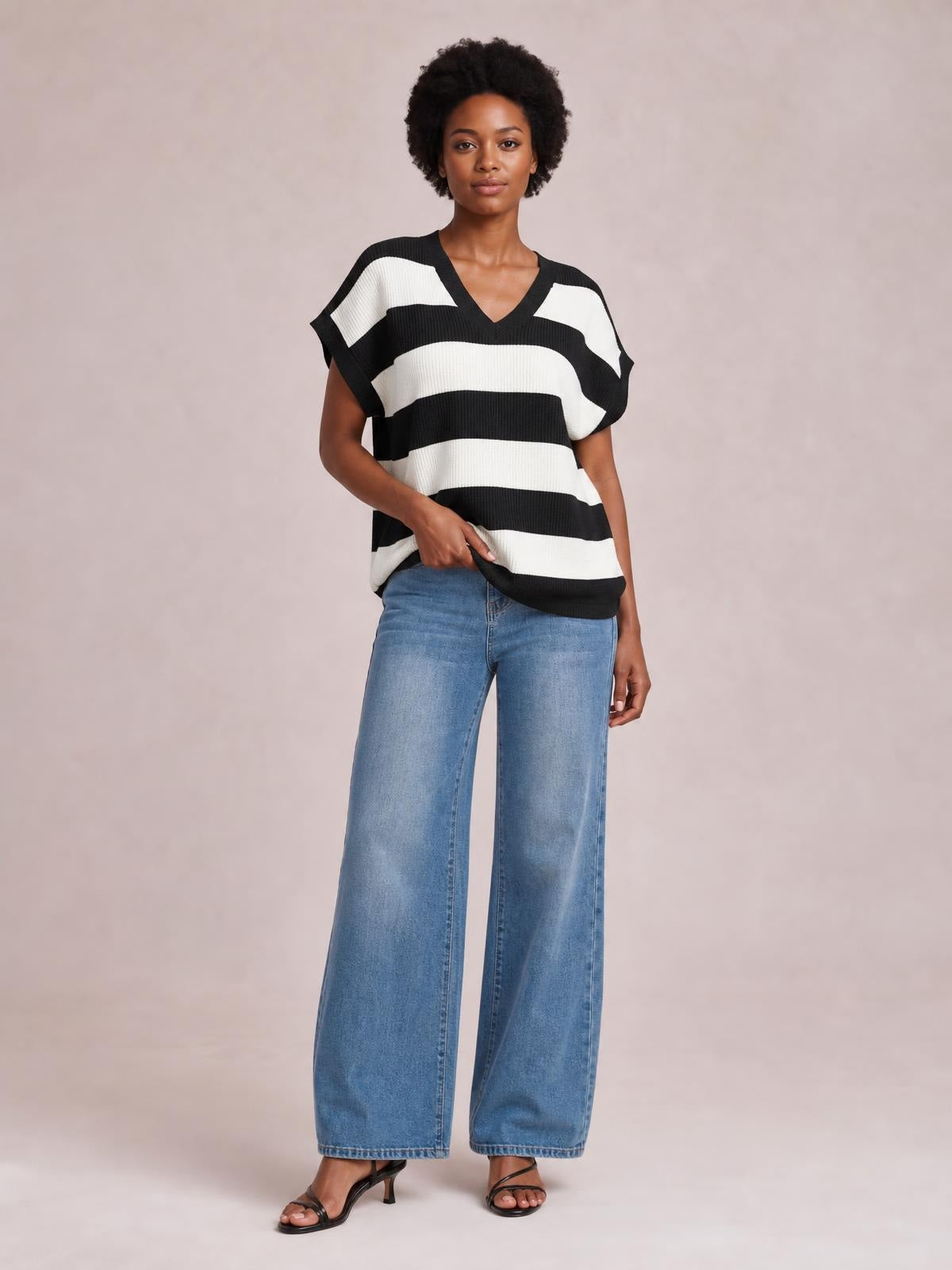 Model wears a black-and-white striped V-neck short sleeve sweater with a relaxed silhouette and ribbed knit texture, gently lifting the hem.
