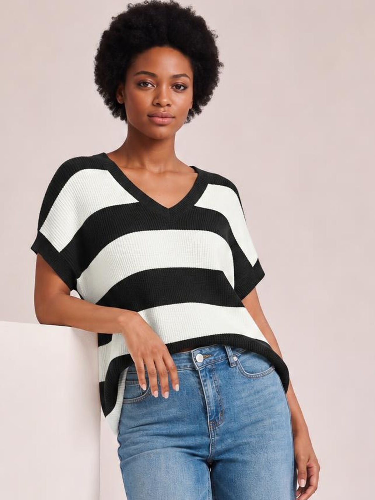 Model wearing a black-and-white striped V-neck short-sleeve sweater with a relaxed silhouette, ribbed construction, and one hand resting on her jeans.
