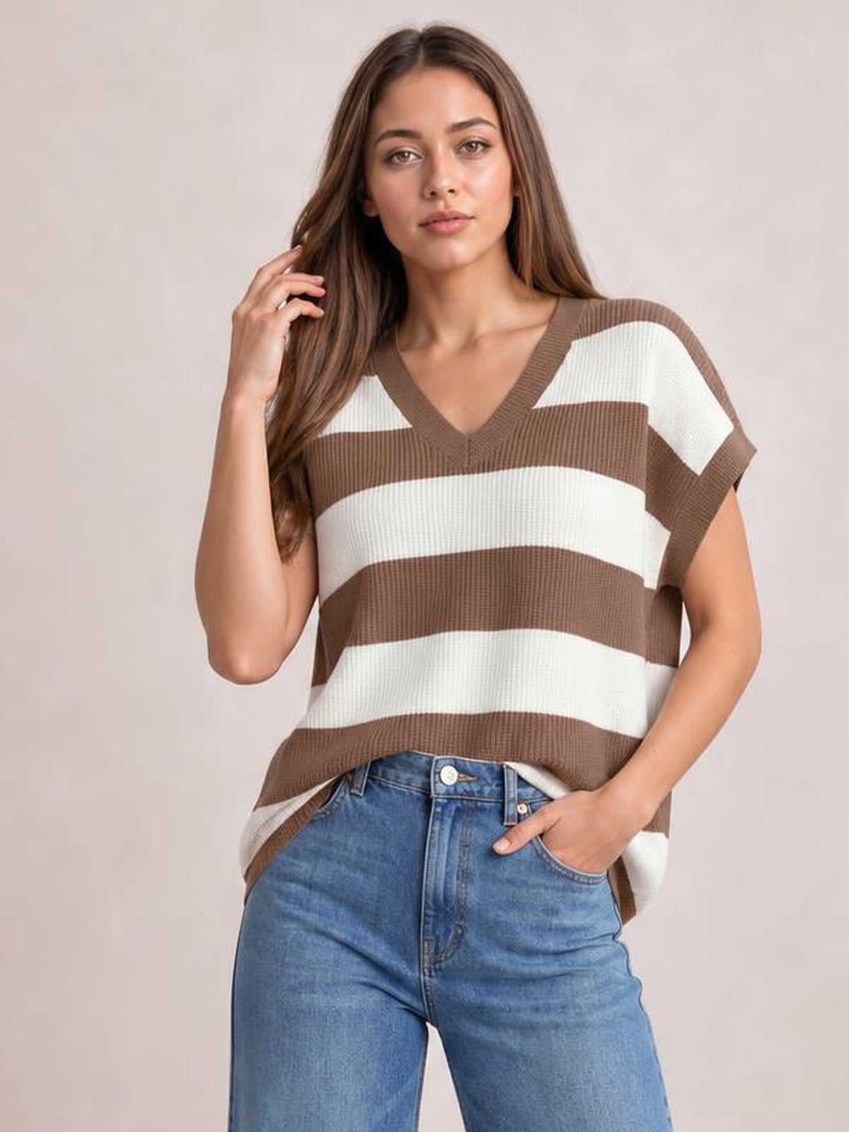 Model poses in a brown and ivory striped V-neck short sleeve sweater with ribbed trim and a relaxed silhouette.