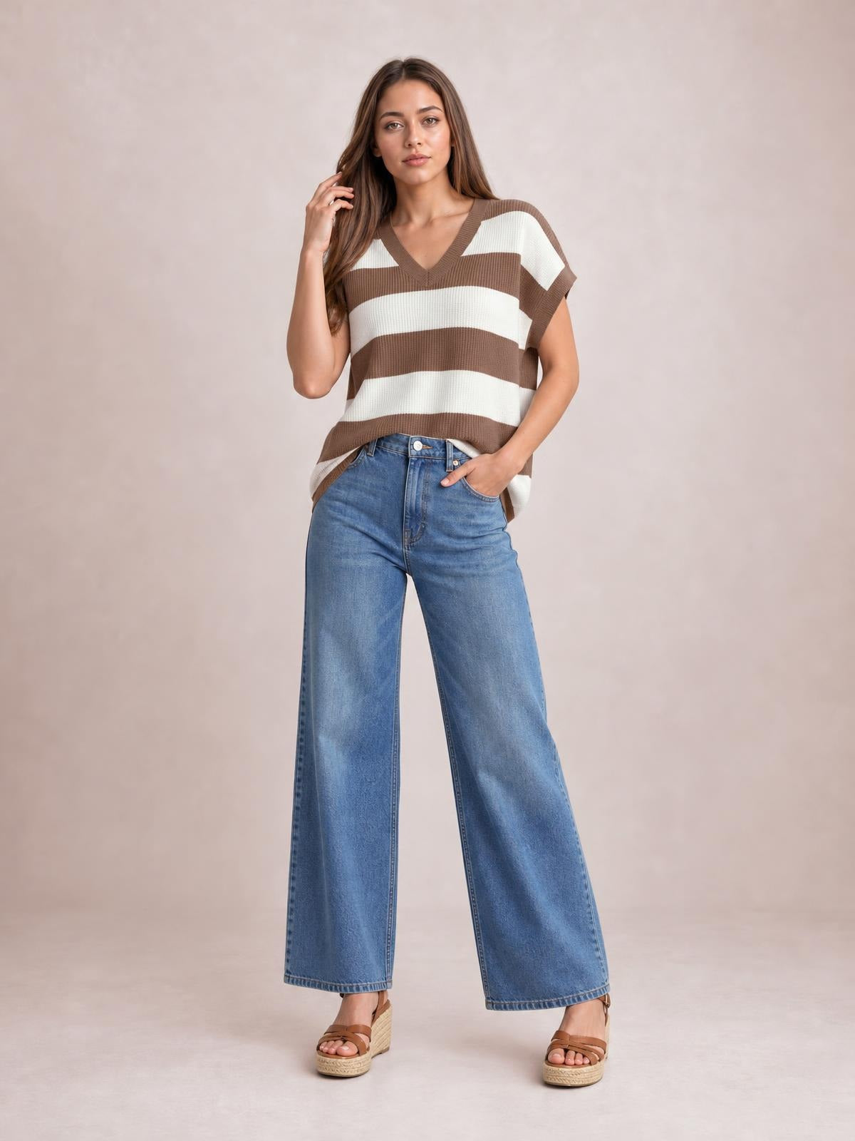 Model poses in a relaxed striped V-neck short sleeve sweater with brown and cream bands, ribbed trim, and a loose silhouette.