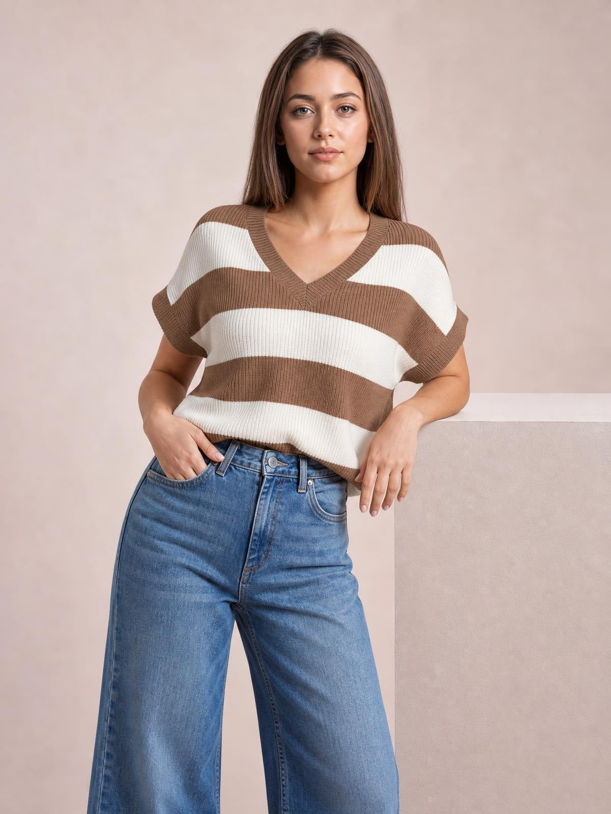 Model wearing a brown and white striped V-neck short sleeve sweater with ribbed trim and a relaxed silhouette, posing with one hand in her jeans pocket.