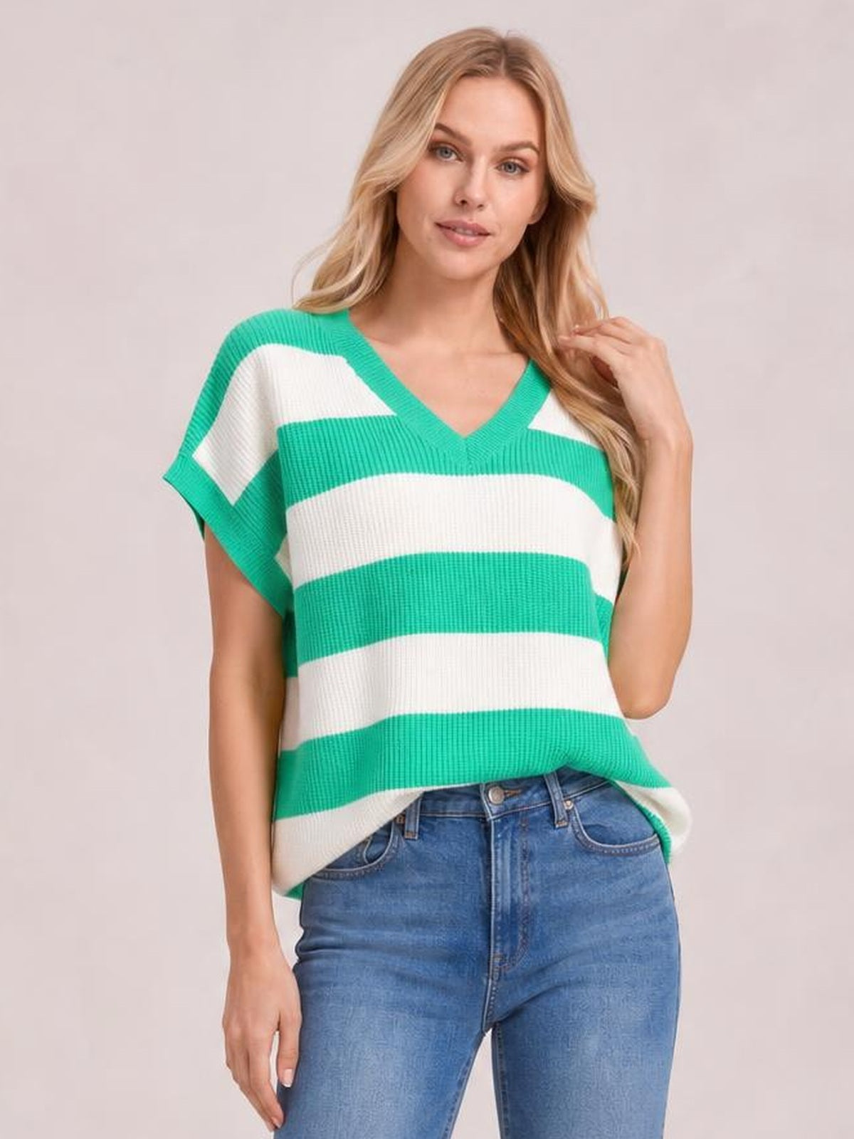 A model poses in a relaxed green-and-white striped V-neck short-sleeve sweater with a loose silhouette and textured knit construction.