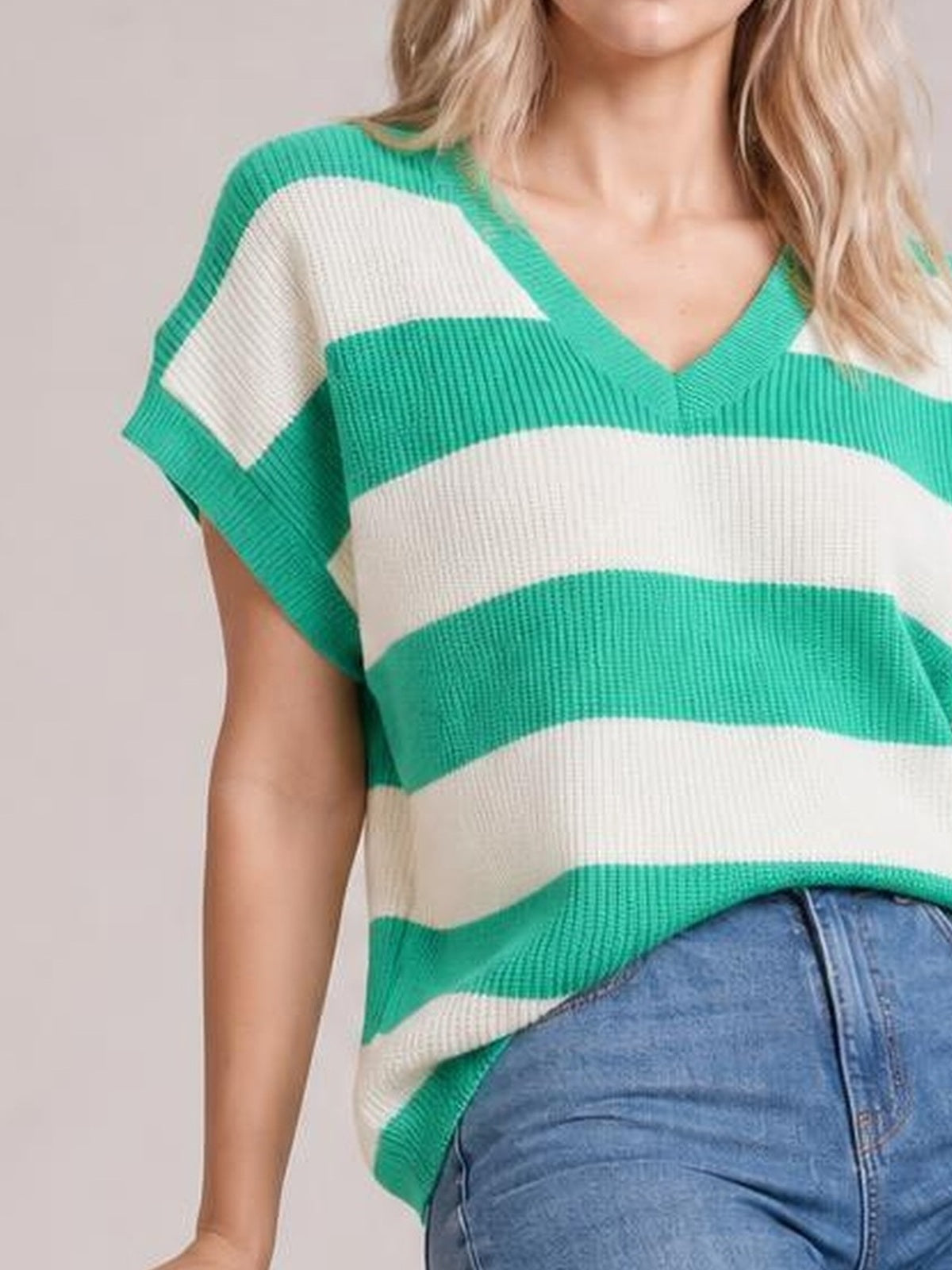 Model poses in a green-and-cream striped V-neck short sleeve sweater with ribbed knit construction and a relaxed silhouette.