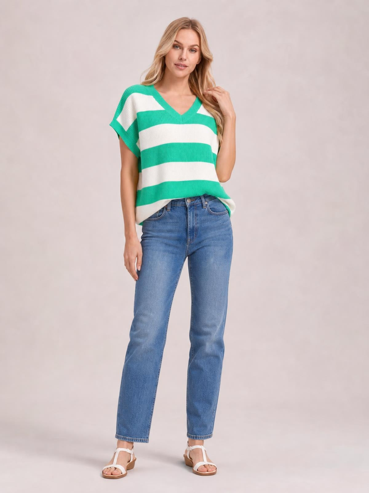 Model wears a green and white striped V-neck short sleeve sweater with a relaxed silhouette and ribbed trim, posing with one hand touching her hair.