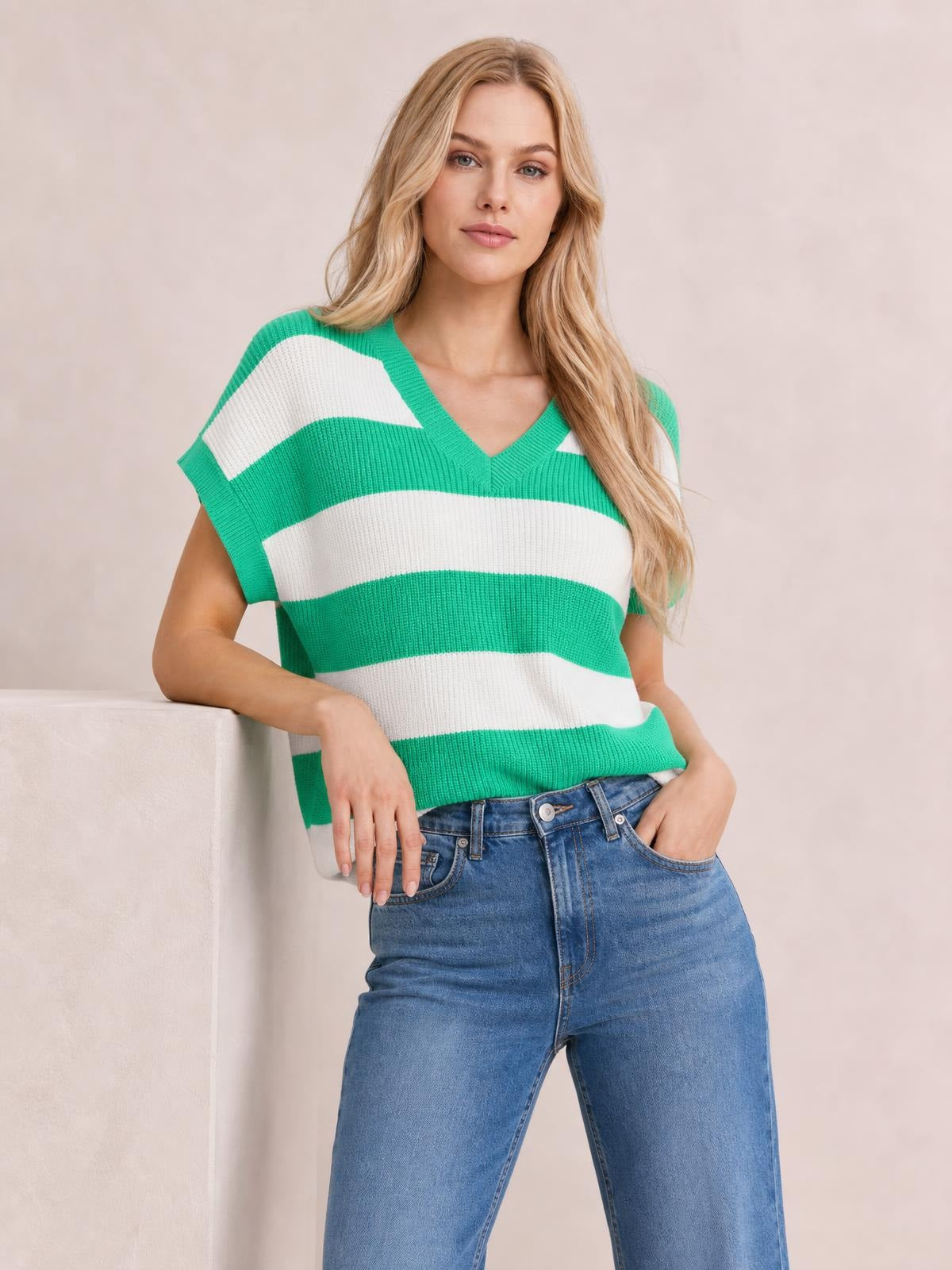 Model leaning with one hand in her jeans pocket, wearing a green-and-white striped V-neck short-sleeve sweater with a relaxed silhouette and ribbed knit trim.