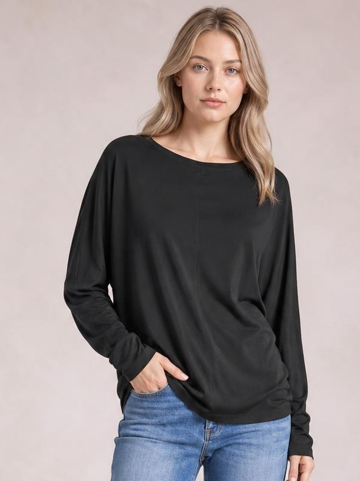 A model wears a black round-neck long-sleeve top with subtle seam detail and a relaxed silhouette, posing with one hand in her jeans pocket.