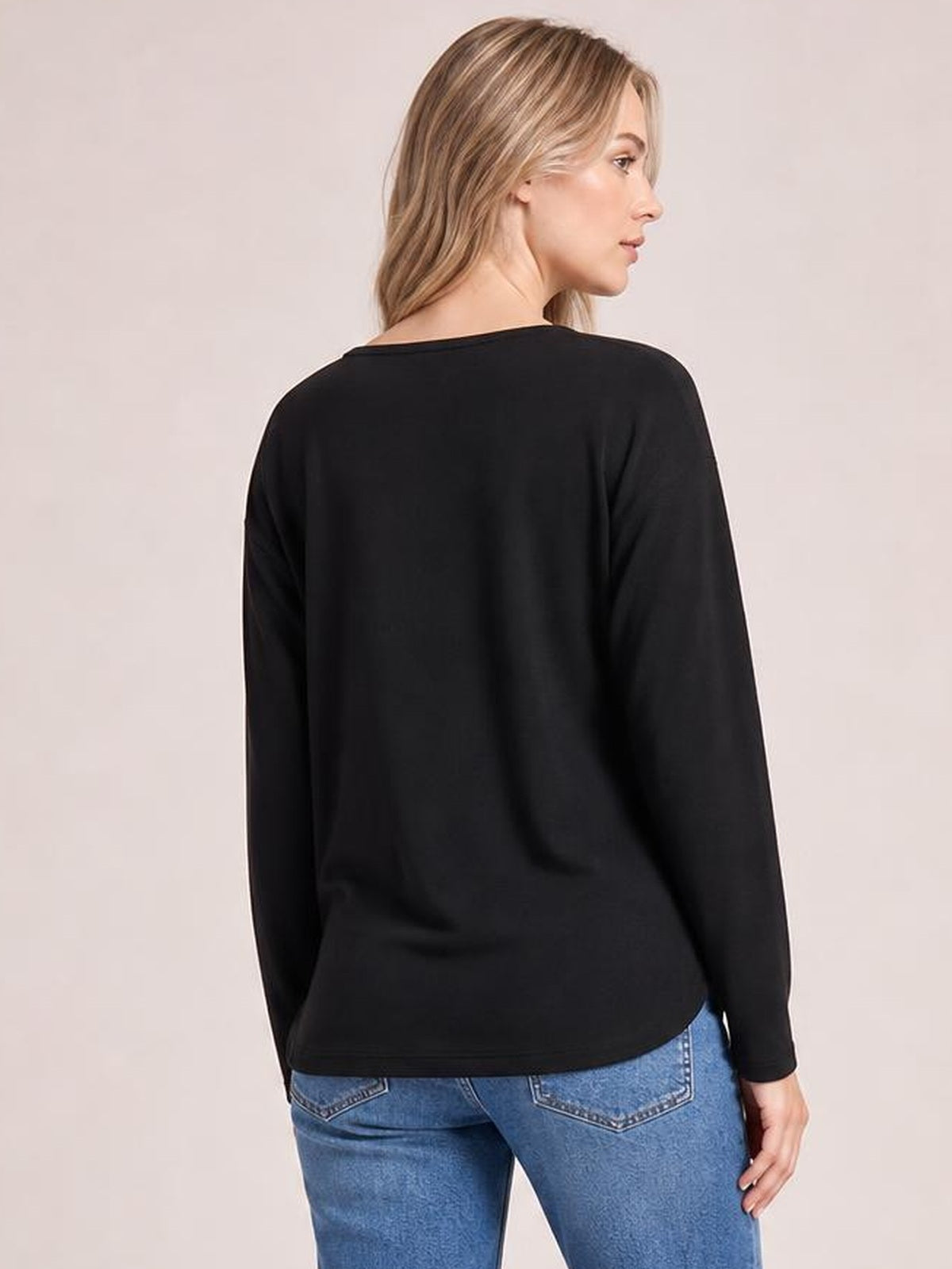 A model looks over her shoulder in a black round-neck long-sleeve top with subtle seam detail and a relaxed, straight silhouette.