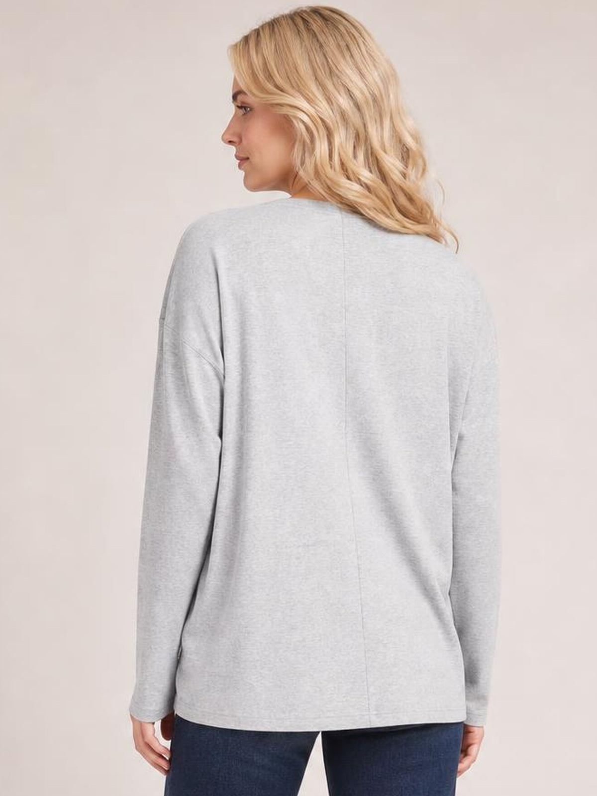 A model looks over her shoulder wearing a light gray long-sleeve top with a relaxed silhouette and visible center-back seam detail.