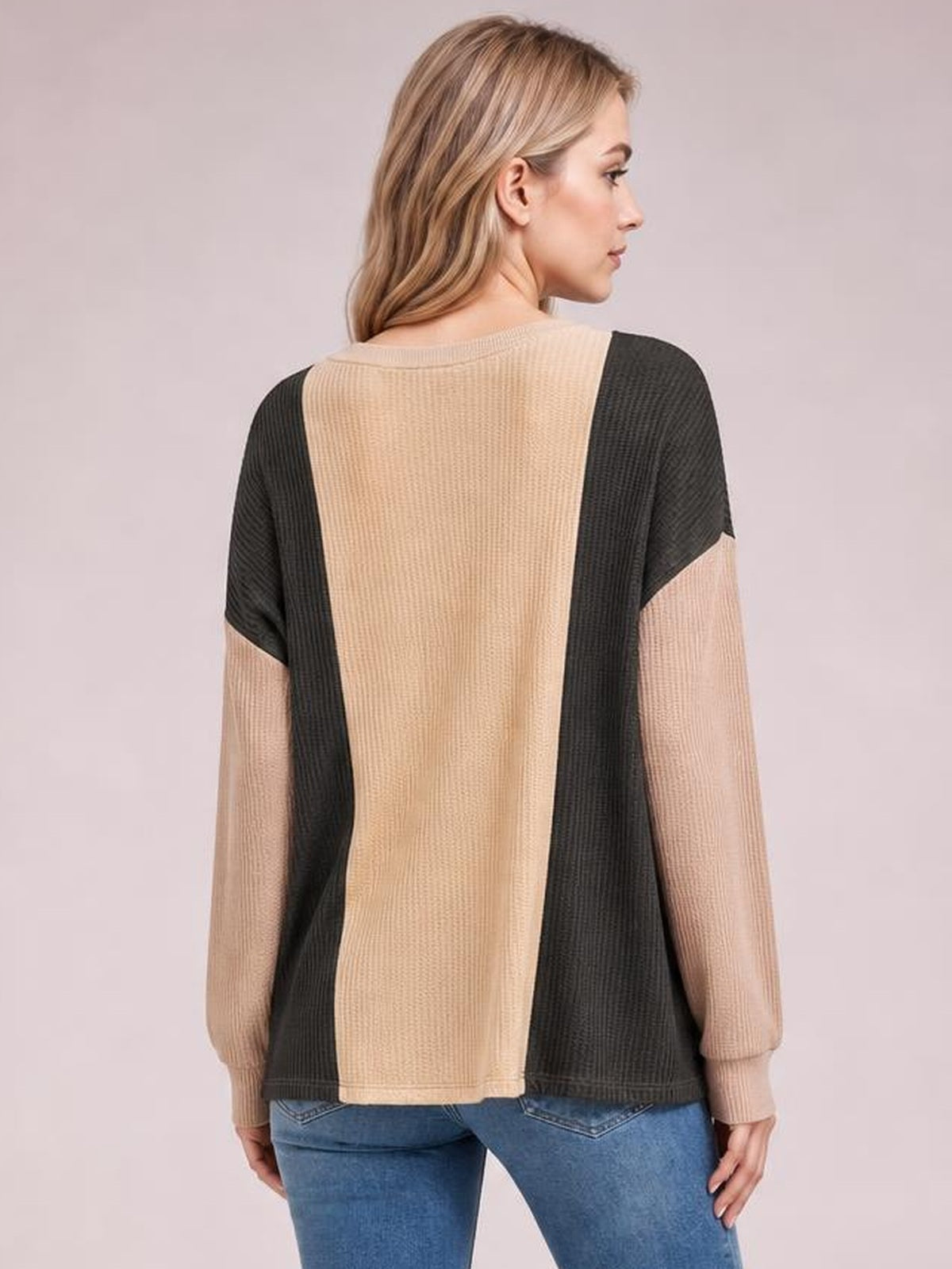 Model shown from behind in a relaxed beige and black texture contrast T-shirt with a round neck, long sleeves, and color-blocked panel construction.