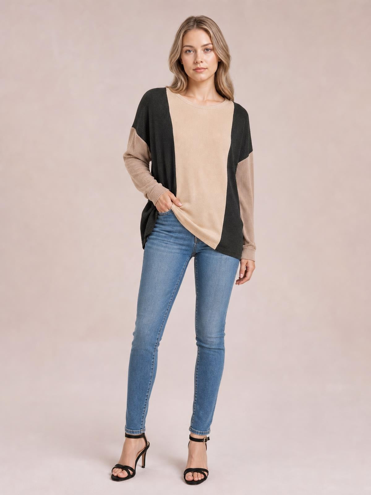 A model stands in a relaxed pose wearing a textured contrast round-neck long-sleeve T-shirt with beige and black color-block panels and a loose silhouette.