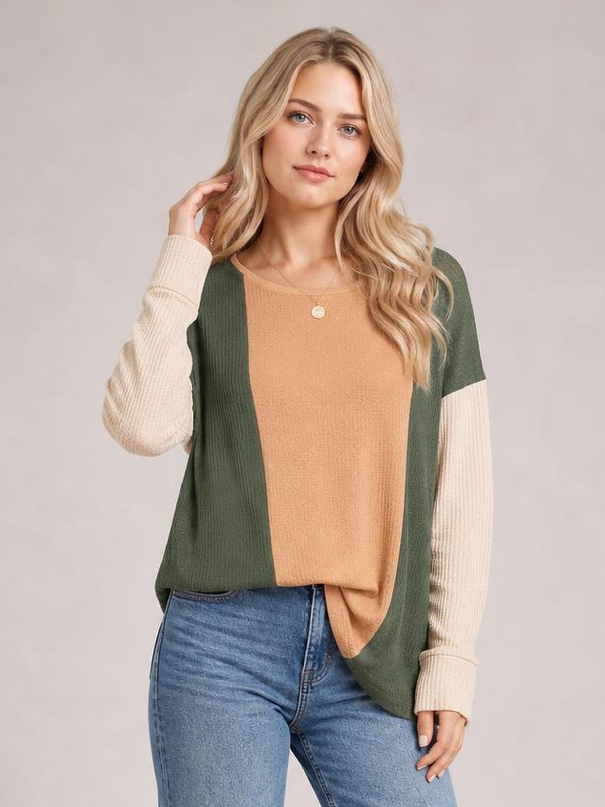 A woman poses in a relaxed-fit texture contrast round neck long sleeve T-shirt with a tan front, olive green sides, and cream ribbed sleeves.