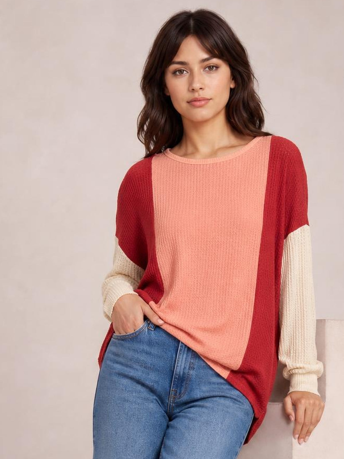 Model poses in blue jeans wearing a relaxed texture contrast round-neck long-sleeve T-shirt with a coral center, red side panels, and cream ribbed sleeves.
