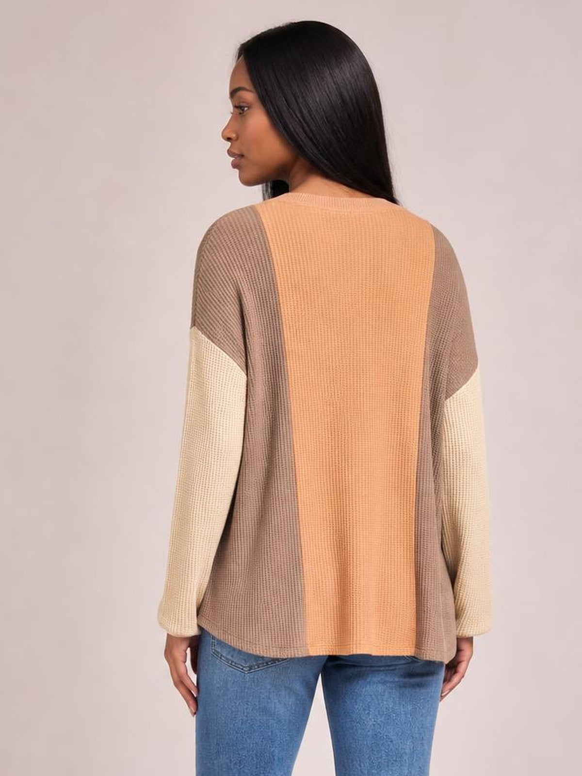 A model faces away in a relaxed, textured contrast T-shirt with a round neck, long sleeves, terracotta center panel, taupe sides, and cream sleeve sections.