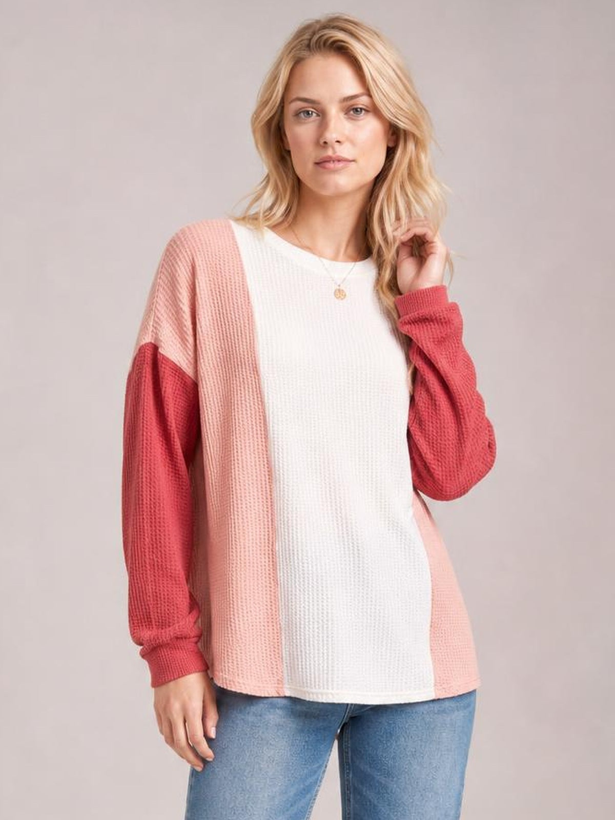 A woman poses in a relaxed texture contrast T-shirt with a white round neck, pink side panels, coral long sleeves, and a loose silhouette.