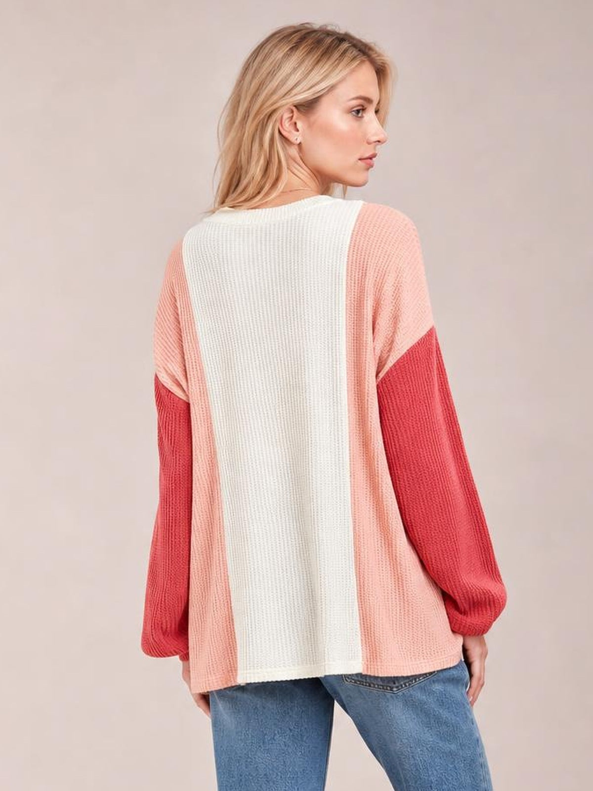 A model turns to show a relaxed texture-contrast long-sleeve T-shirt with a round neck, cream center panel, blush sides, and deep coral sleeves.
