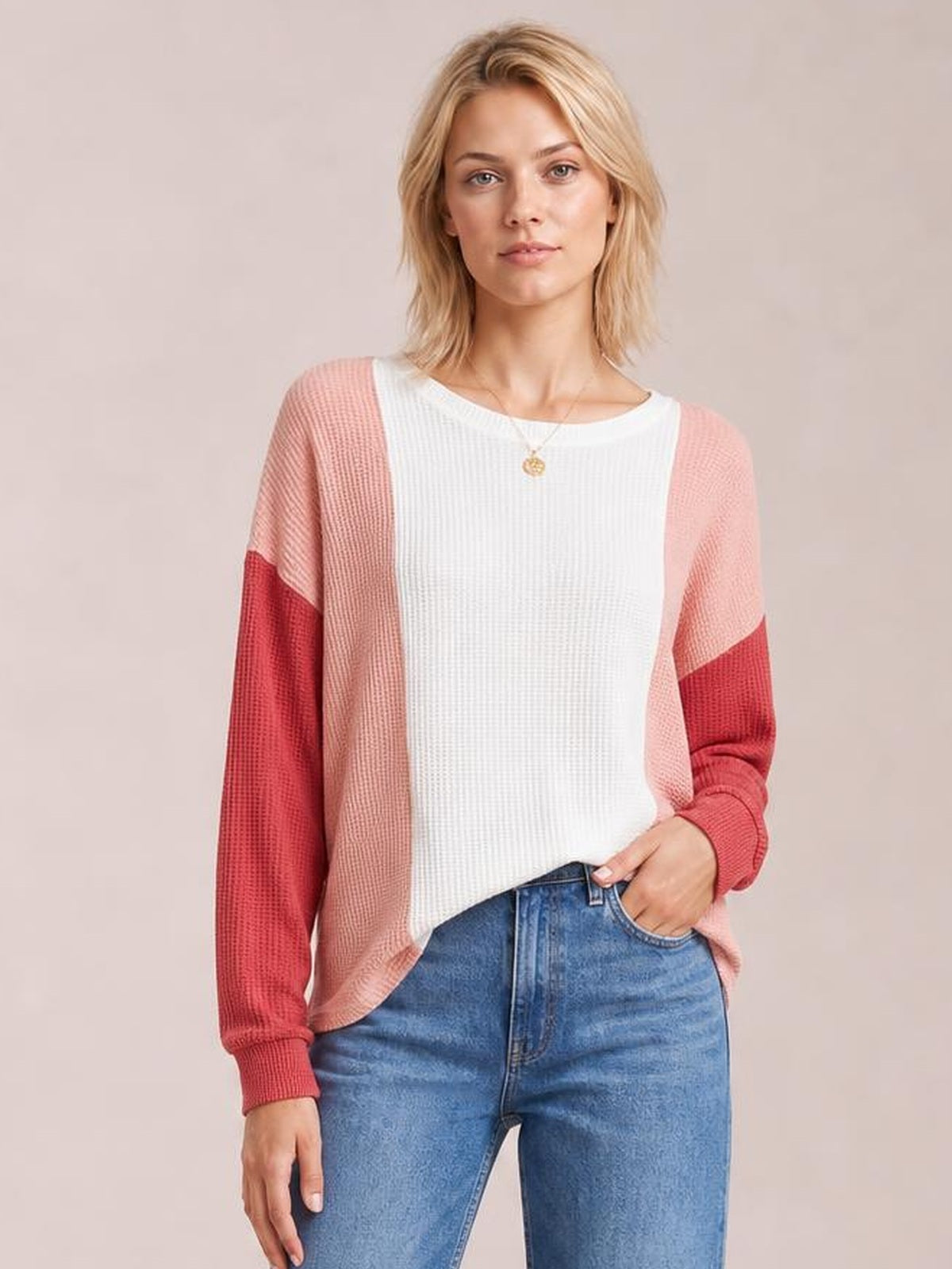 Model wearing a textured color-block long sleeve T-shirt with a white round neck, blush pink body panels, and red sleeves, posing with one hand in her jeans pocket.