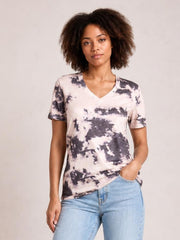 Model wearing a pink and charcoal tie-dye V-neck T-shirt with short sleeves, a relaxed straight silhouette, and a slightly curved hem while posing with one hand in her jeans pocket.