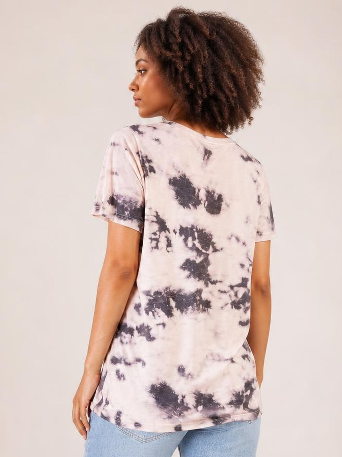 Model turned away to show a relaxed-fit tie-dye V-neck T-shirt in pale pink with dark abstract patches, short sleeves, and a straight hem.