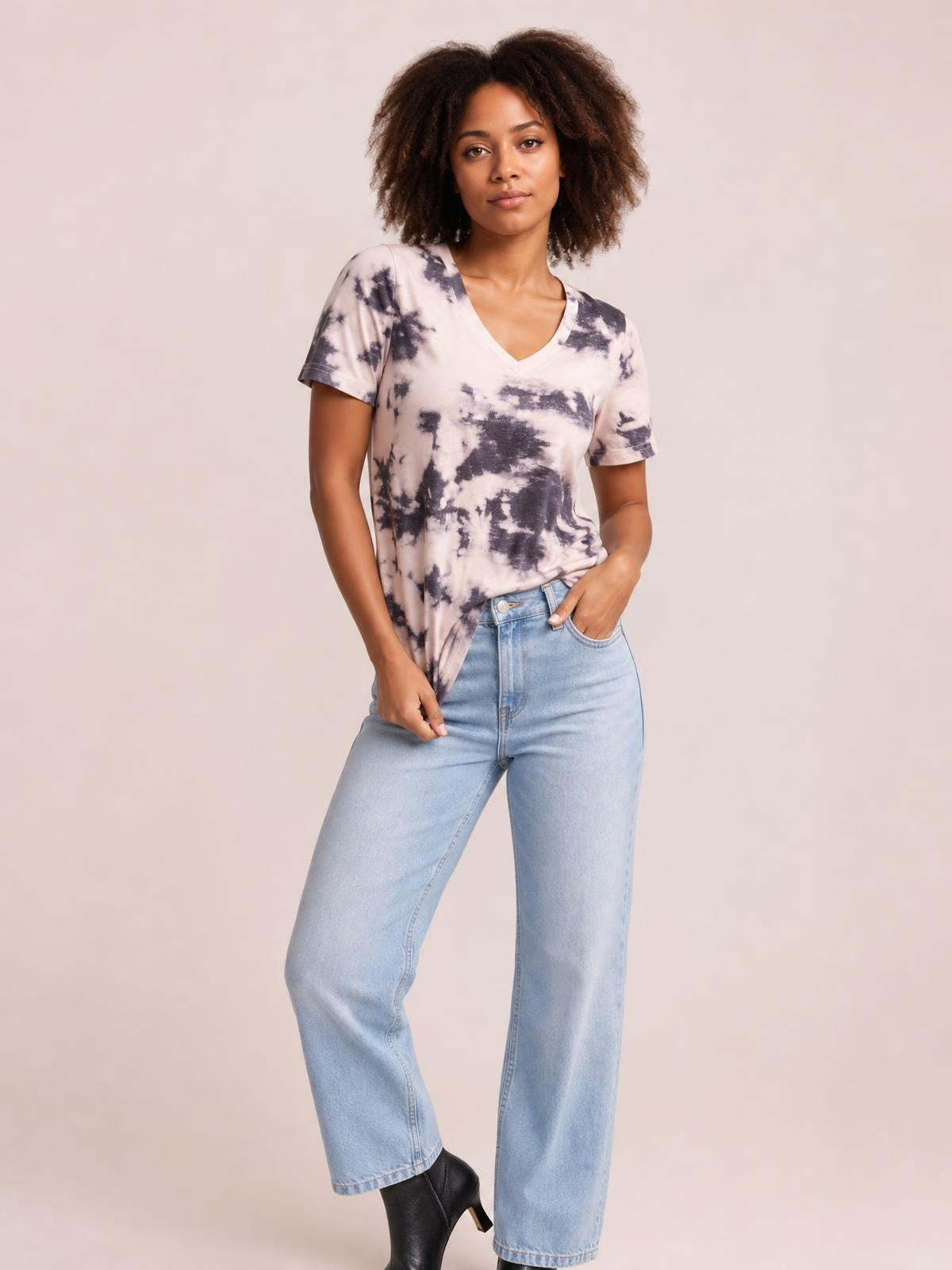 Model wears a pink and charcoal tie-dye V-neck T-shirt with short sleeves and a relaxed straight silhouette, lightly tucked into jeans.