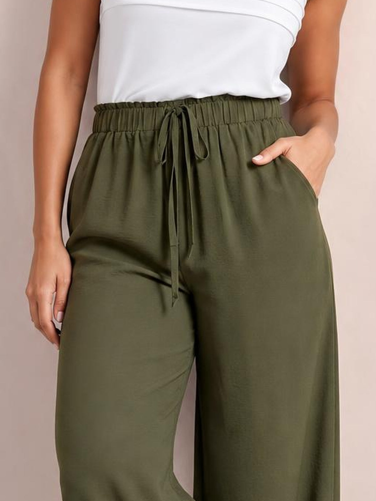Model in a white top wears olive-green drawstring wide-leg pants with an elastic waistband, relaxed silhouette, side pockets, and one hand tucked into a pocket.