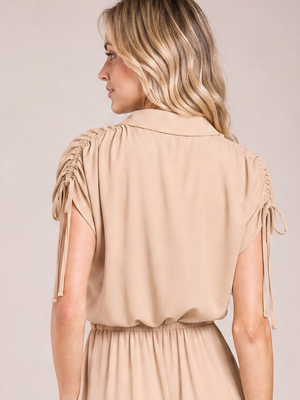 Model turned over her shoulder wears a beige collared midi dress with short ruched sleeves, drawstring ties, a gathered waist, and a softly flared skirt.